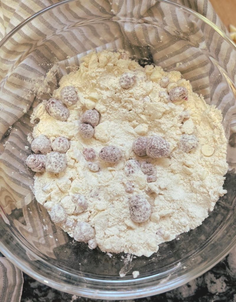 White chocolate and raspberries mixed into flour in a glass bowl.