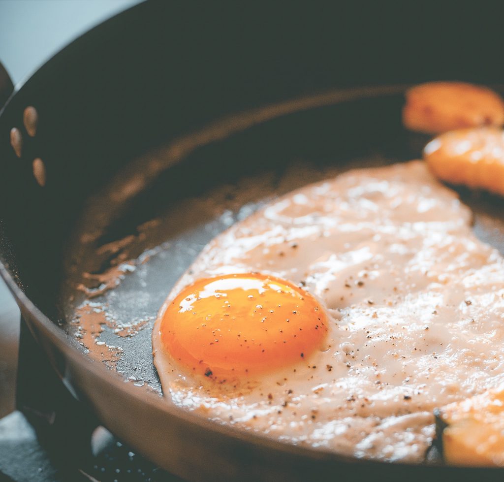 An egg and potatoes cooking in a nonstick pan.
