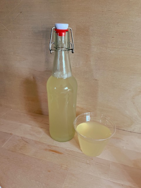 A swing top bottle and a cup full of hydrating lemonade on a wooden counter top.