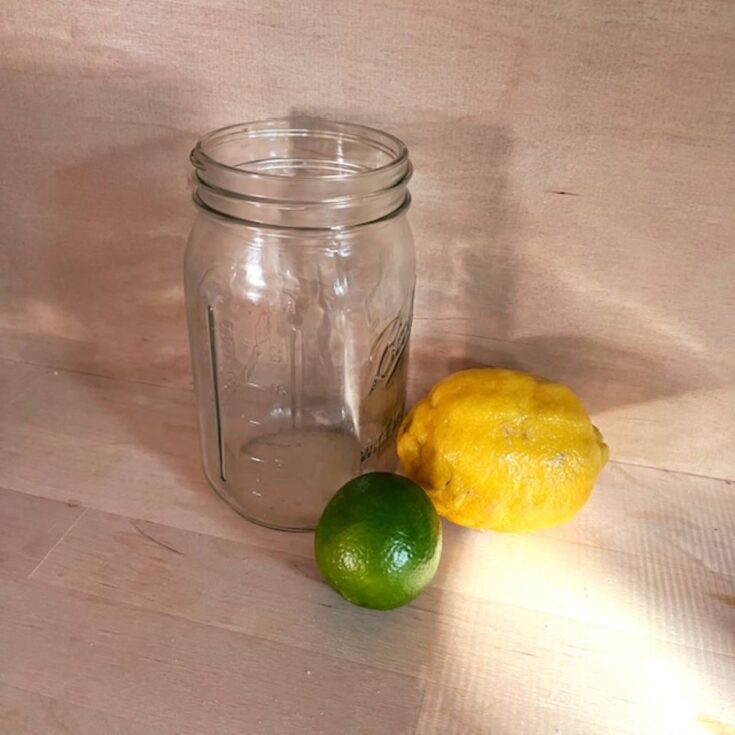 A quart sized mason jar, a lemon, and a lime on a wooden counter top.
