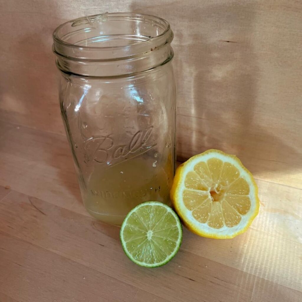 A quart sized jar next to a half a lemon and half a lime on a wooden counter top.