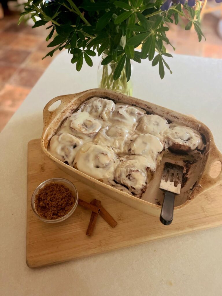 A pan of cinnamon rolls with a bouquet of flowers on a white countertop.