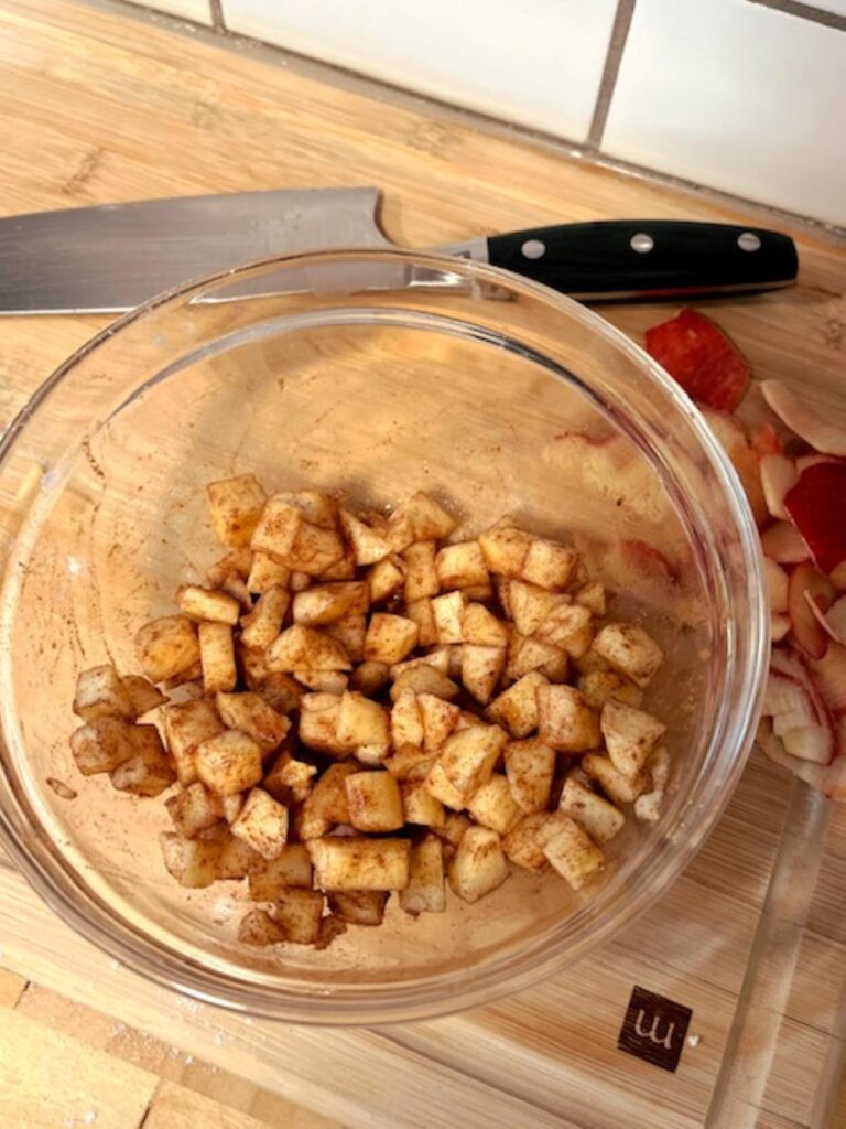 Small diced apples tossed with cinnamon and honey in a glass bowl on a cutting board.