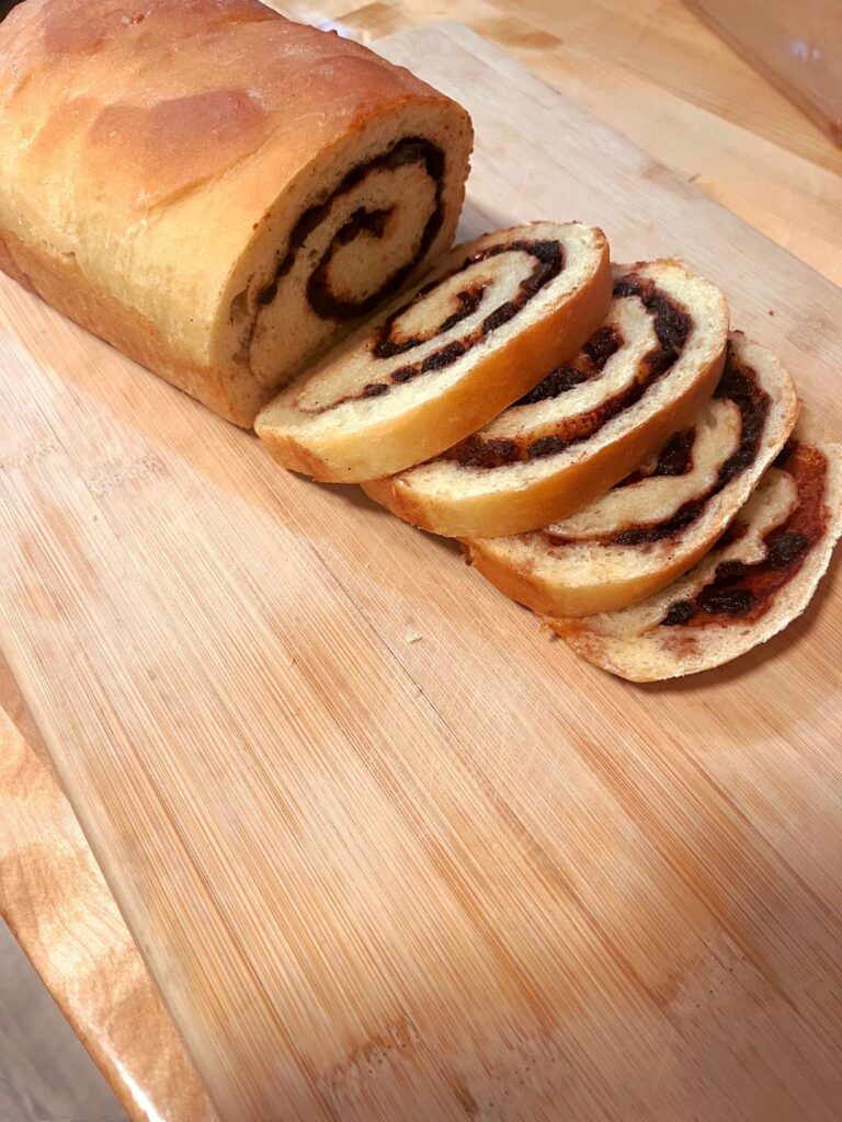Raisin cinnamon bread freshly sliced on a wooden cutting board.