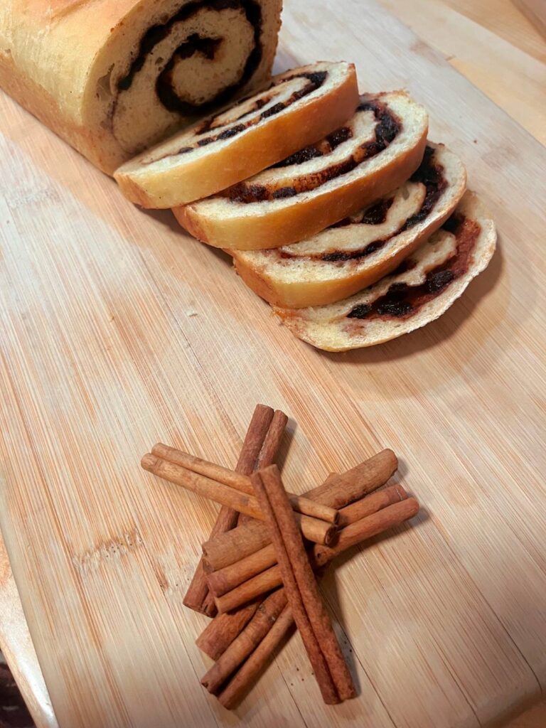 Raisin Cinnamon bread on a wooden cutting board with cinnamon sticks