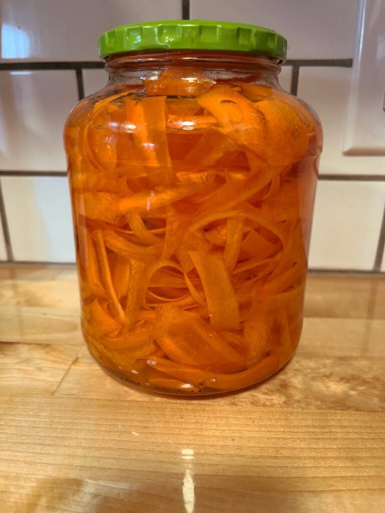A jar full of ribboned carrots ready to be turned into a raw carrot salad