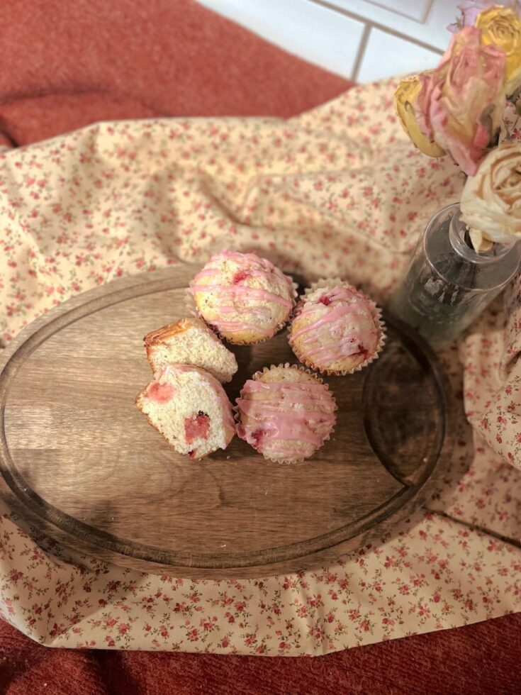 Strawberry vanilla sourdough muffins on a dark wood cutting board. With dried roses and a