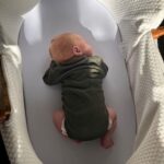 A baby in a green onesie in a basket