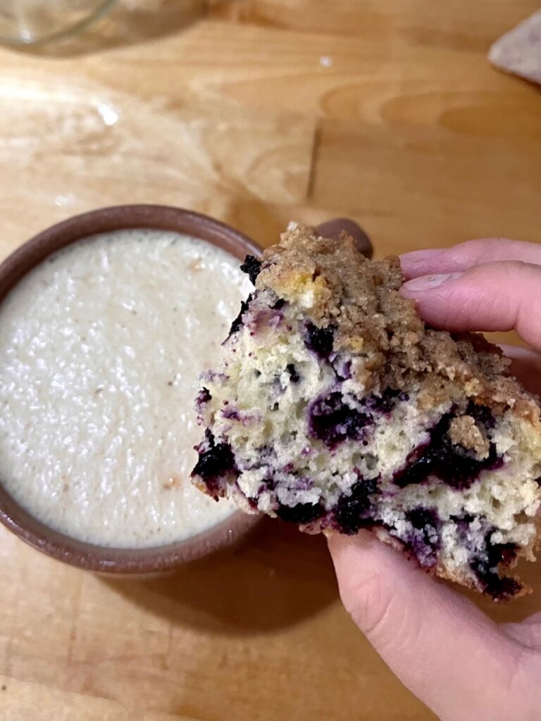 A slice of coffee cake being held over a cup of coffee.