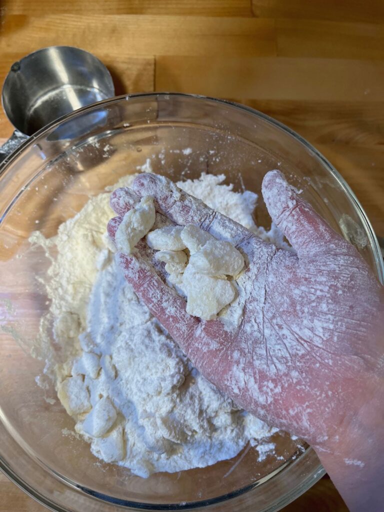 Chunks of butter held in a hand above a bowl of butter and flour