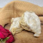 Two glazed scones on a cutting board with a red rose.