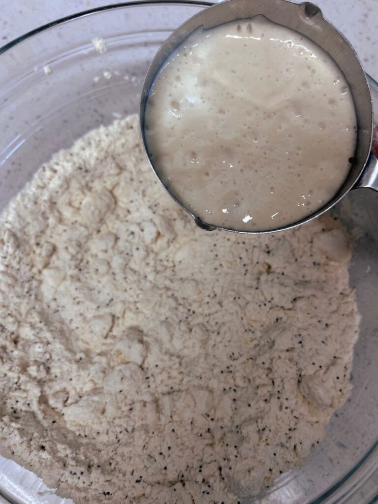 A measuring cup of sourdough discard held over a bowl of butter and flour.