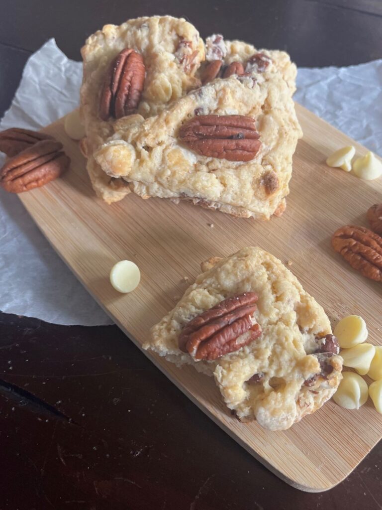 A small stack of white chocolate pecan sourdough scones on a small wooden cutting board.