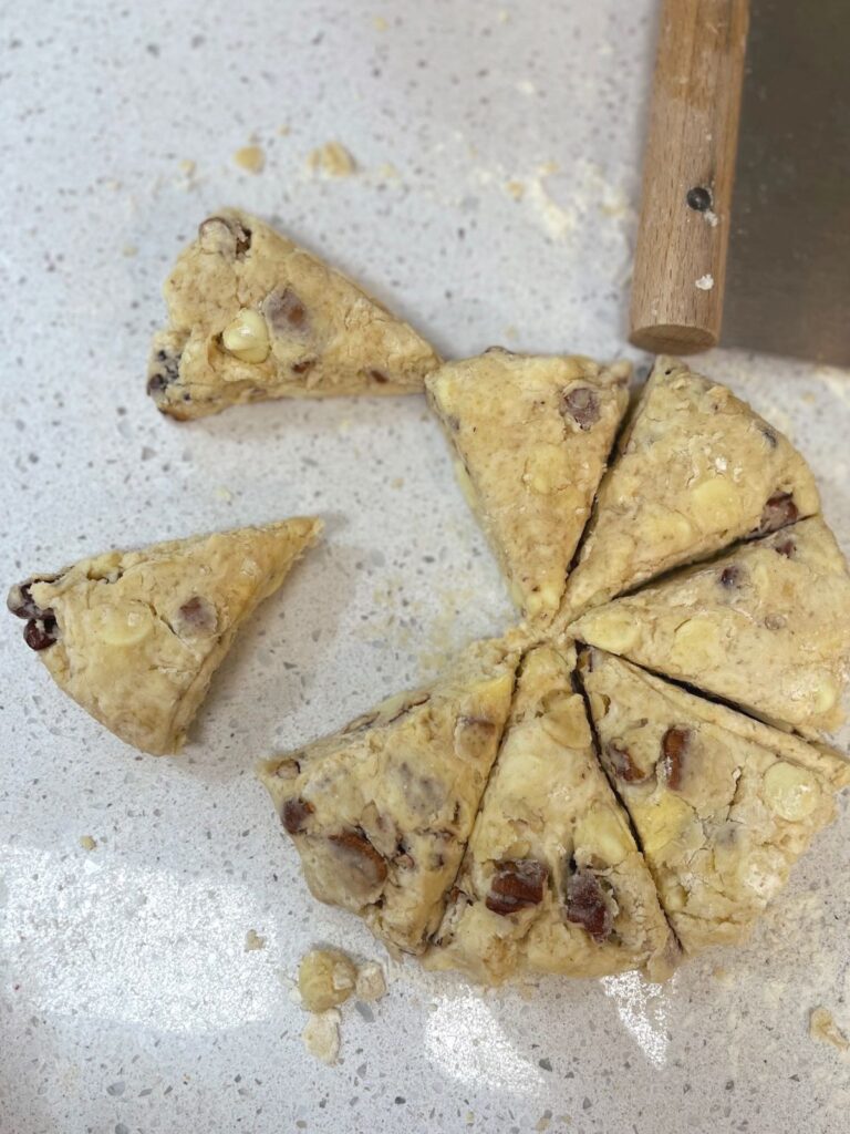 A disk of scone dough divided into 8 equal parts on a countertop with a bench scraper.