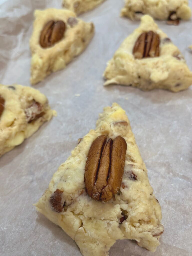 White chocolate pecan sourdough scones each topped with a whole pecan on a sheet tray ready for the oven.