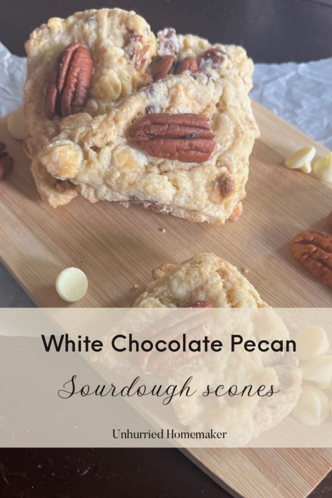A pile of scones on a cutting board with pecans and white chocolate chips all around.