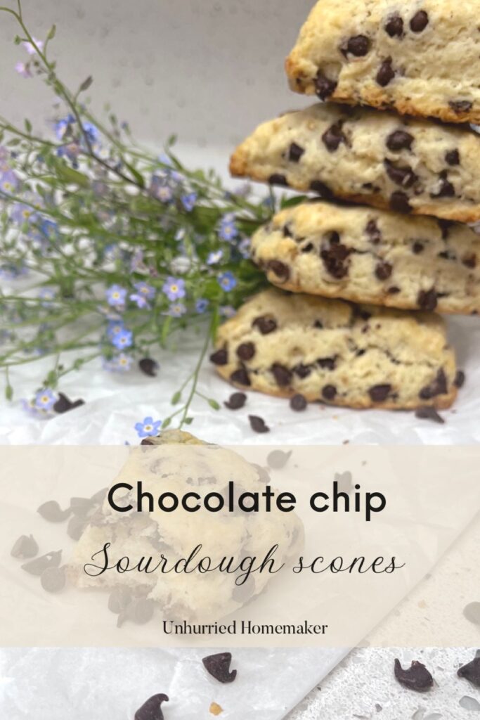 A scone with a bite taken out of it in front of a stack of more chocolate chip scones and some blue flowers.