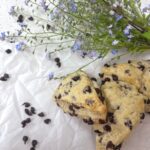 Two chocolate chip sourdough scones on parchment paper next to a bouquet of forget me not flowers.