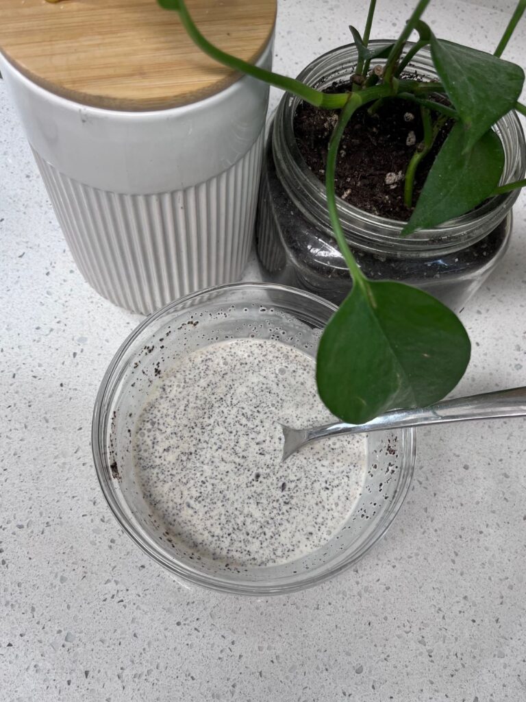 A bowl of cream mixed with coffee grounds next to a coffee canister and a plant in a jar.
