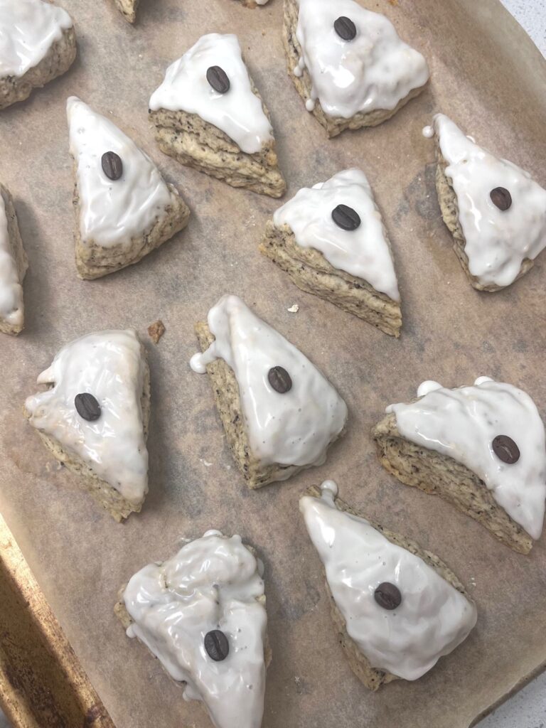 Freshly glazed sourdough scones on a sheet tray, each of the scones has a coffee bean in the center of the glaze.