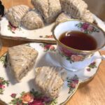 A tea cup and saucer with two earl grey sourdough scones drizzled with glaze.