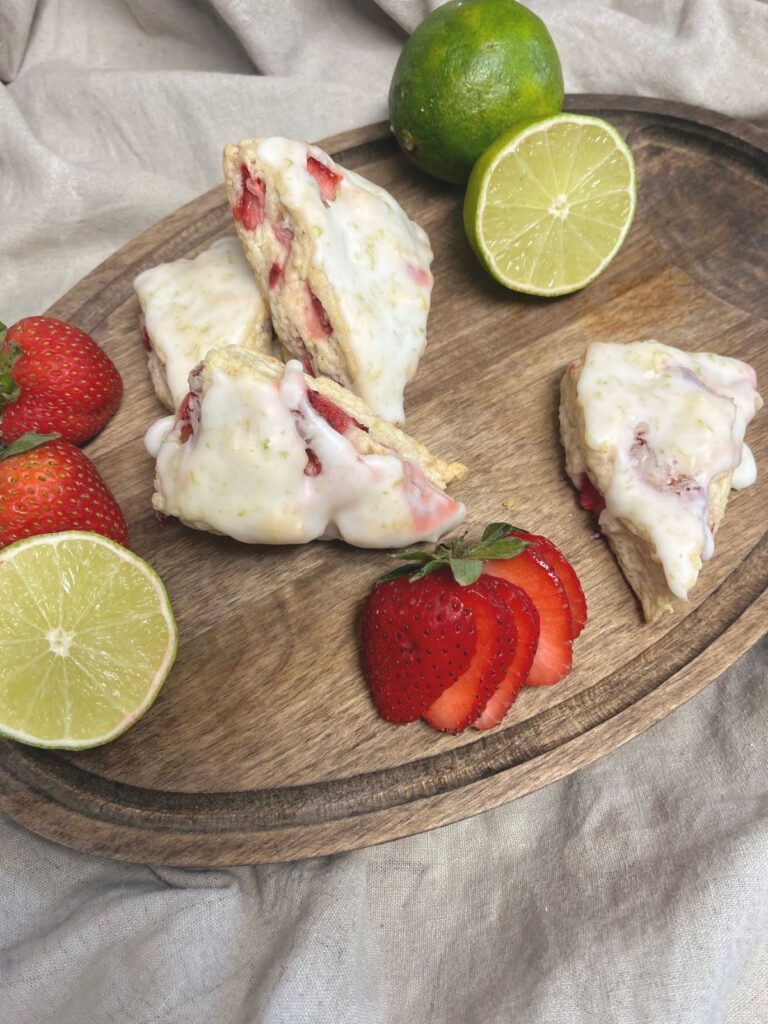 Scones on a cutting board with sliced strawberries and the halves of limes.