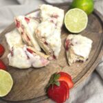 A pile of strawberry lime sourdough scones on a wooden cutting board with sliced limes and strawberries all around
