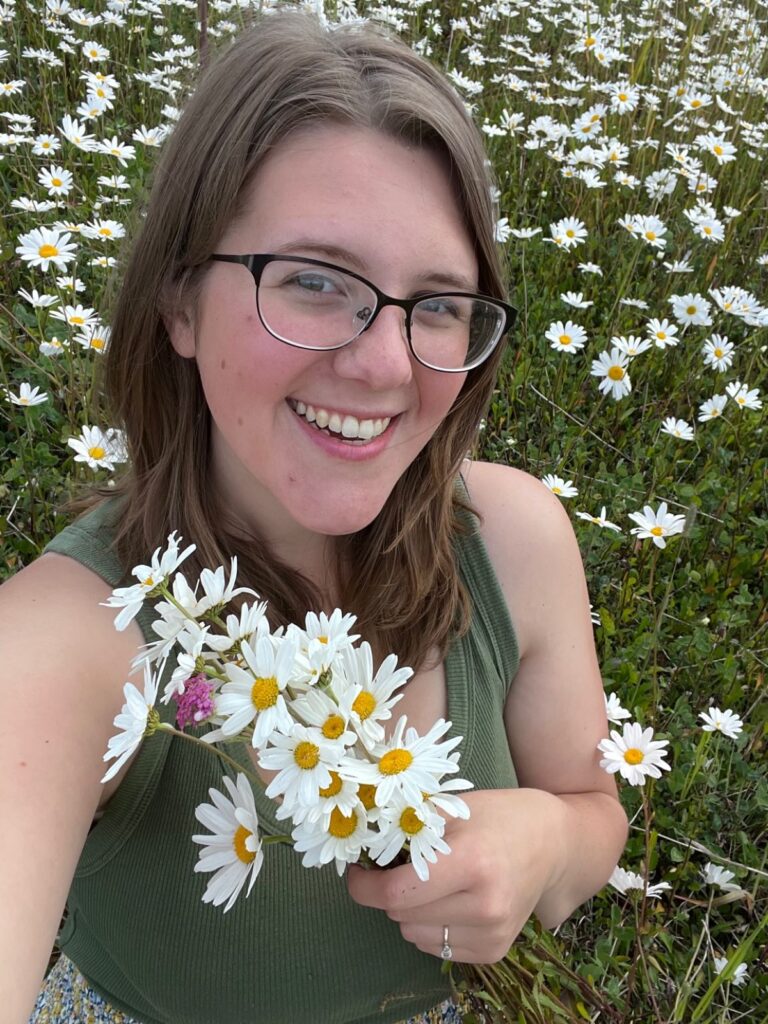 Unhurried homemker holding a bouquet of fresh daisies in a green tank-top and smiling up at the camera.