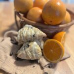 A basket of oranges behind a stack of glazed sourdough scones.
