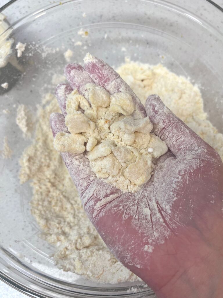 A flour covered hand holding a pile of butter chunks covered in flour.