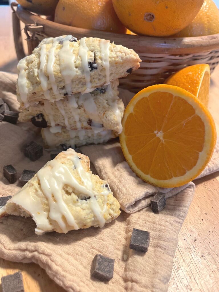 A chocolate orange sourdough scone with a bite taken out of it surrounded by citrus.