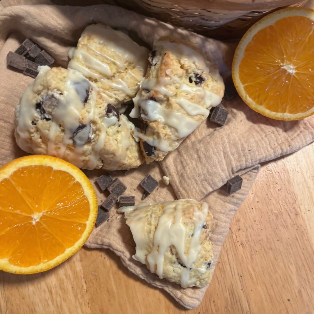 A pile of scones on a cloth with oranges and chocolate chunks all around it.