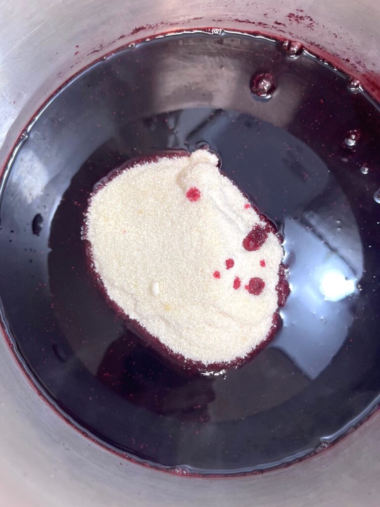 A pot with a pile of sugar and dark purple juice.