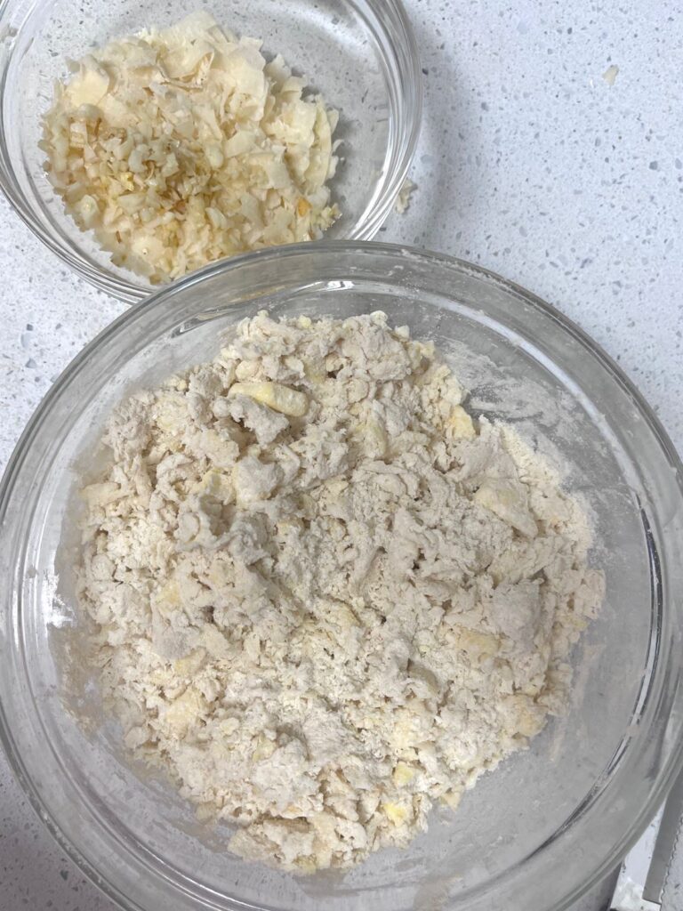A bowl of dry ingredients and a bowl of grated cheese and garlic on the side.