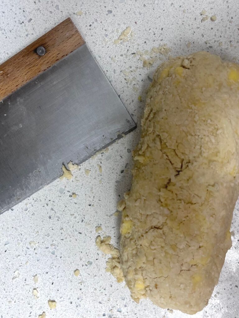 A log of sourdough scone dough on a counter with a bench scraper.