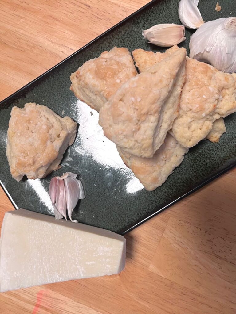 A long green plate with a wedge of parm on the side, a small stack of scones and some garlic.