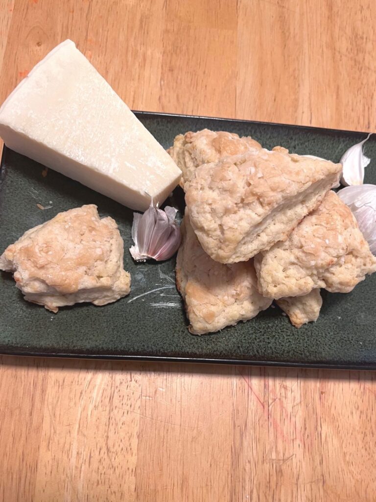 A green plate with a pile of scones, a wedge of parmesan, and a few cloves of garlic.