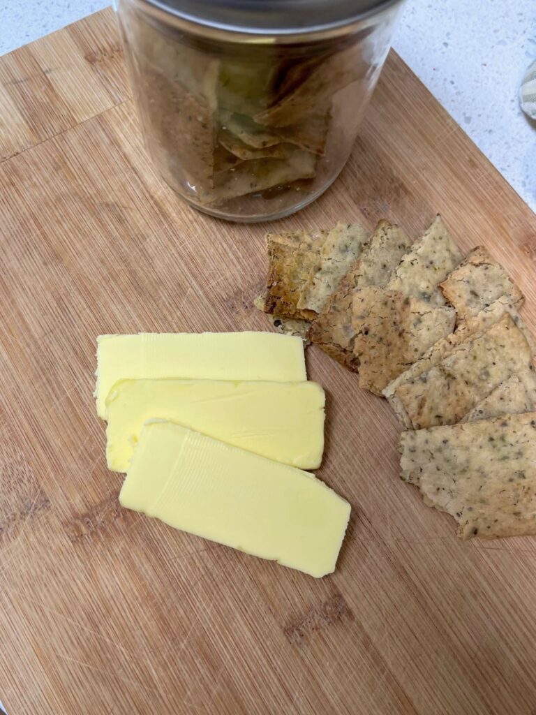 A jar of crackers on a cutting board with slices of cheese and more crackers next to the jar.