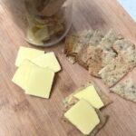 A jar of sourdough discard crackers on a cutting board with crackers and cheese next to it.