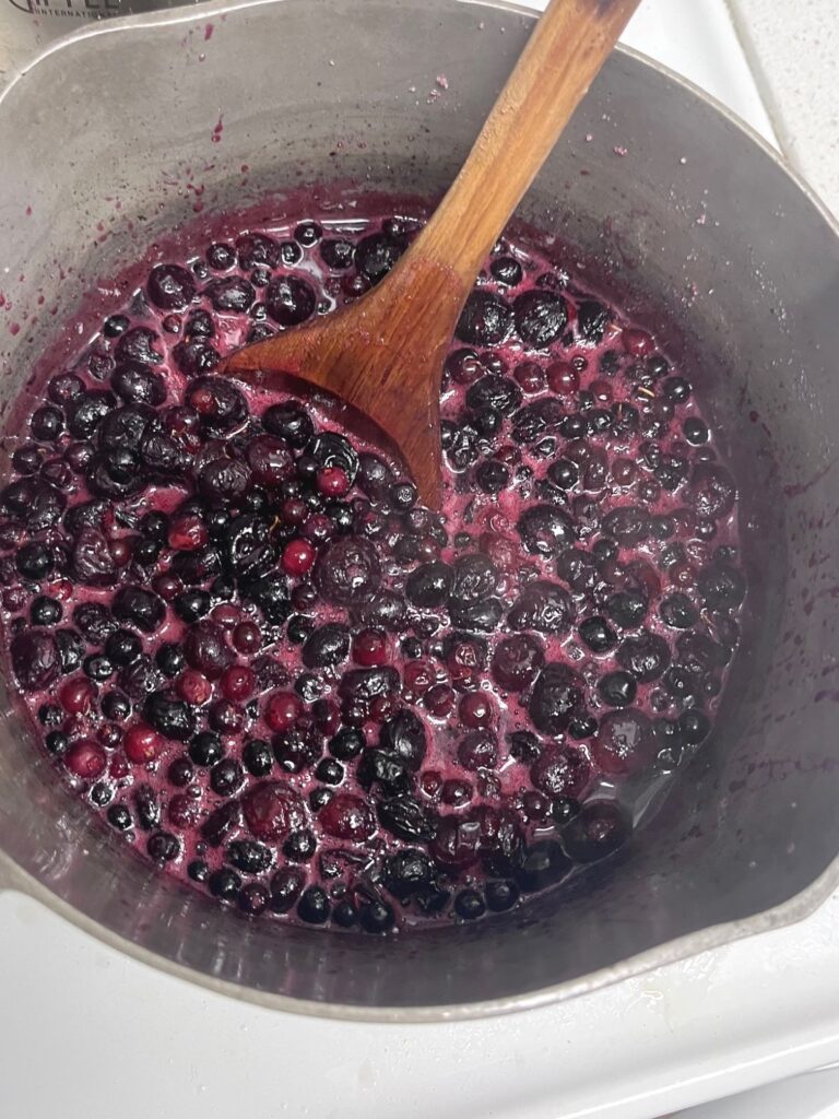 Blueberry jam in a pot with a wooden spoon.
