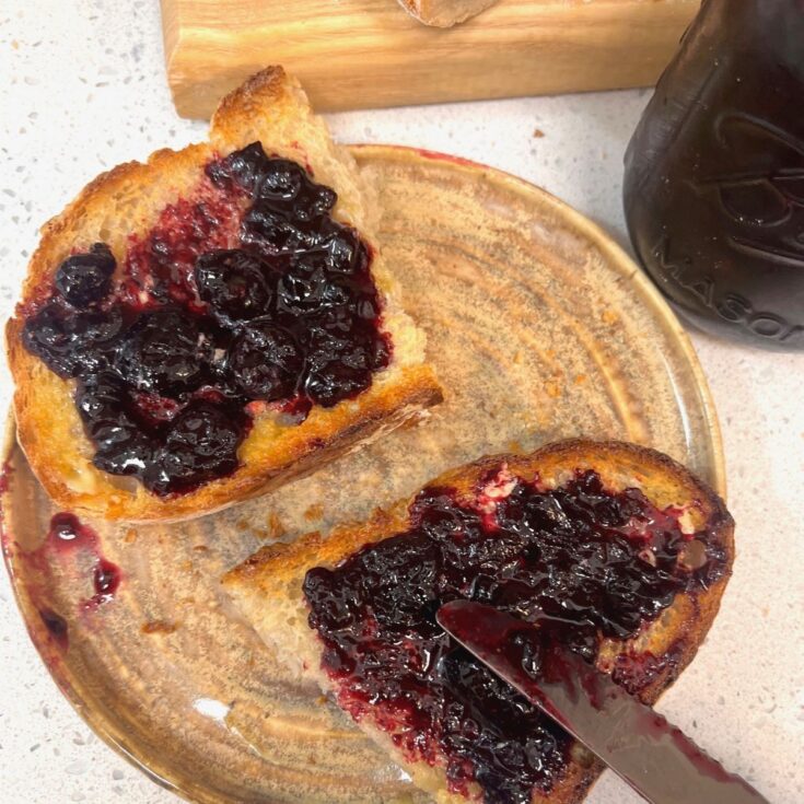 Two halves of a slice of sourdough bread spread with homemade blueberry jam.