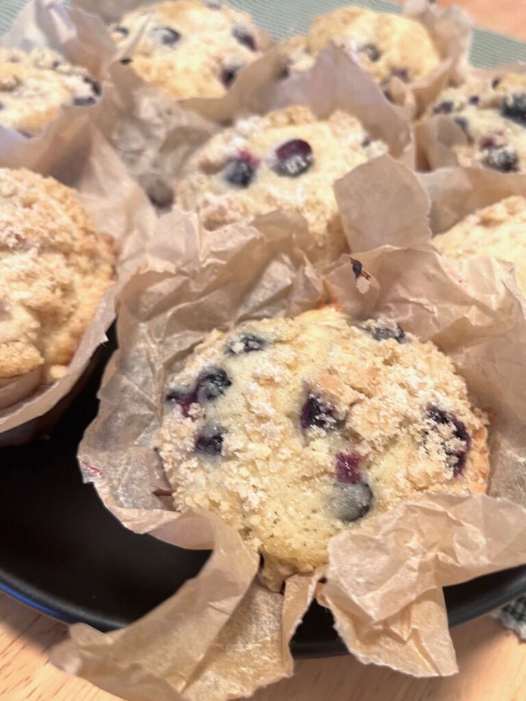 Blueberry muffins in parchment paper wrappers on a black plate.