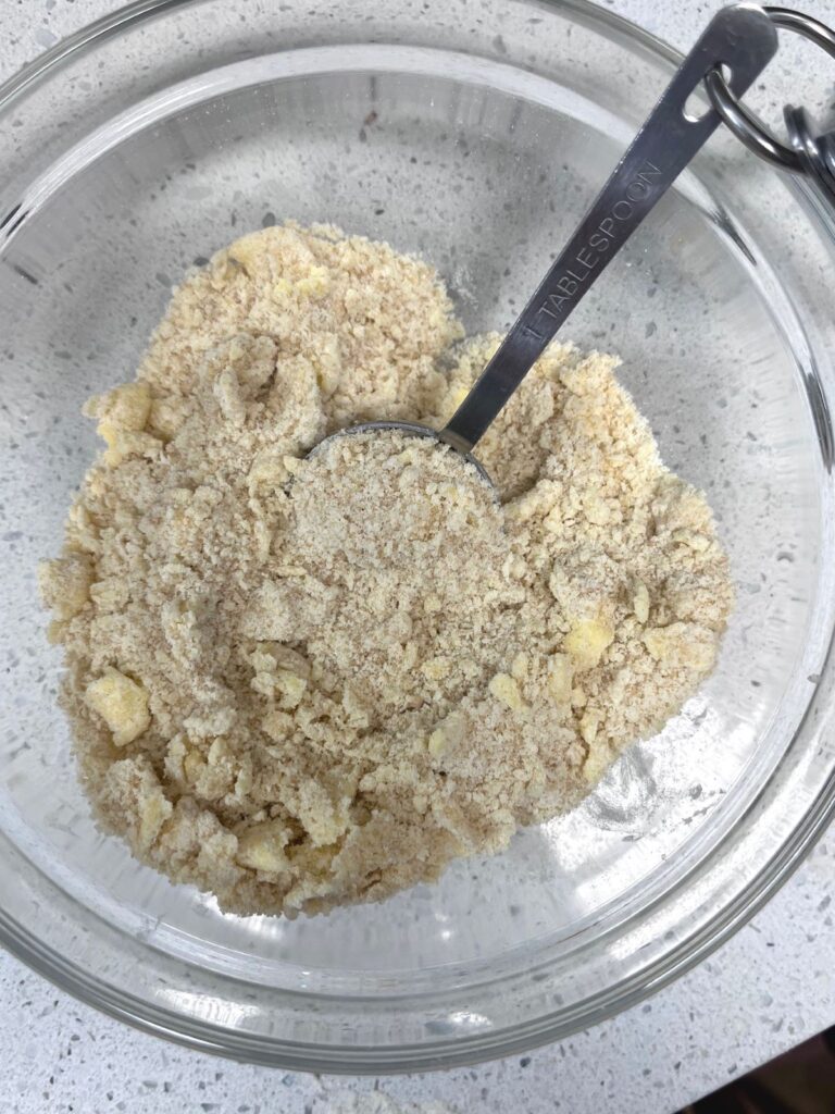 A bowl full of crumb topping with a tablespoon in it. 