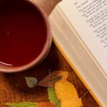 A mug of crabapple mulled cider next to a pile of pressed fall leaves and a book of poems.