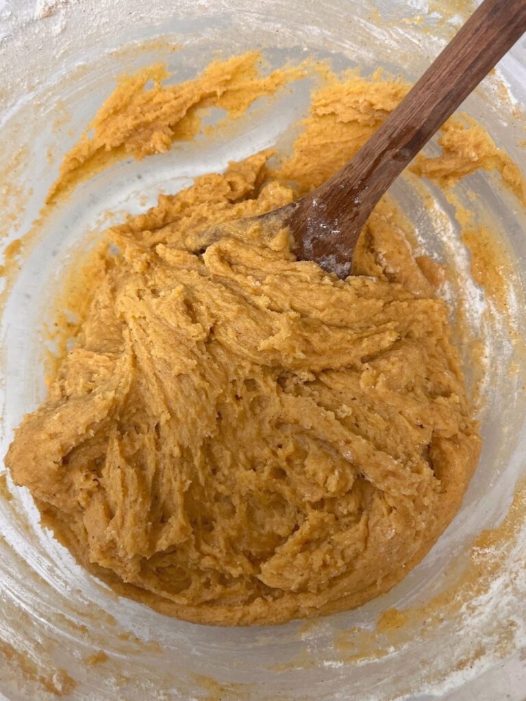 A bowl of pumpkin sourdough snickerdoodle cookie dough with a wooden spoon. 