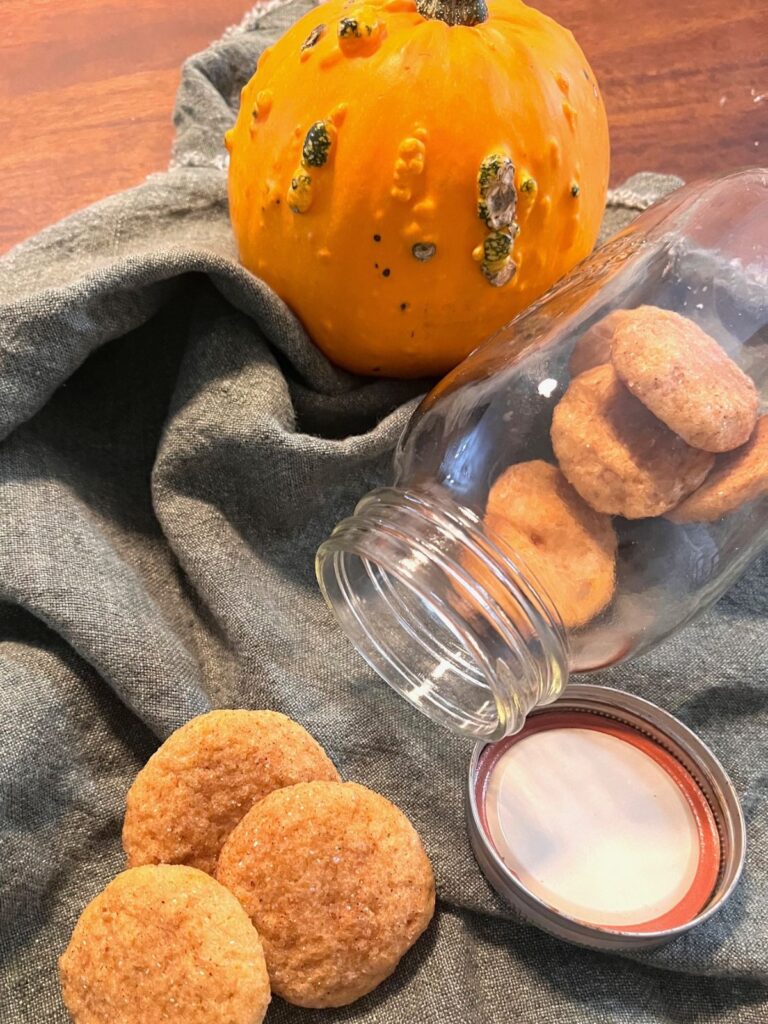 A bumpy pumpkin and a jar of cookies spilling out onto a green cloth napkin. 