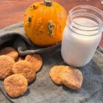 Pumpkin sourdough snickerdoodles on a green cloth napkin with a small pumpkin and a jar of milk.