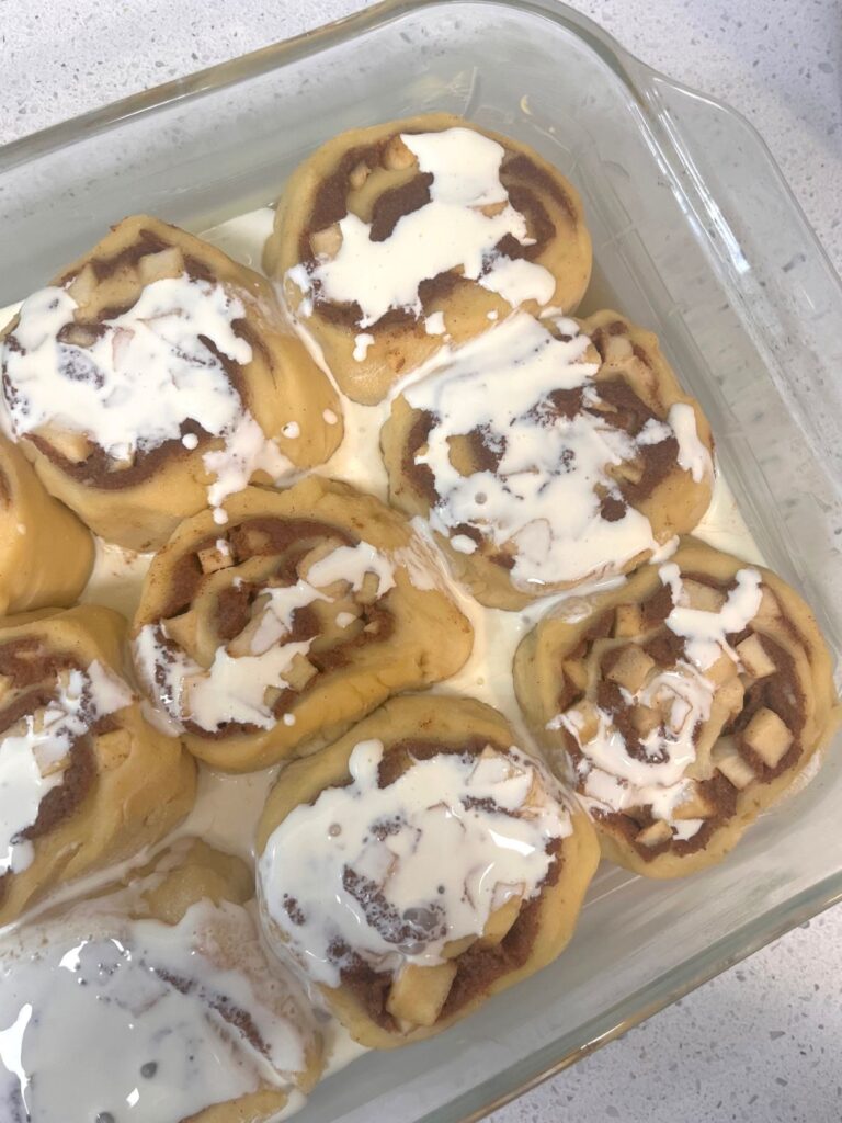 Unbaked cinnamon rolls in a baking dish drizzled with cream.