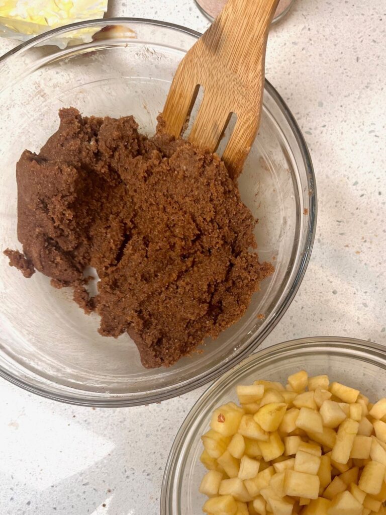 A bowl of cinnamon roll filling next to a bowl of small diced apples.