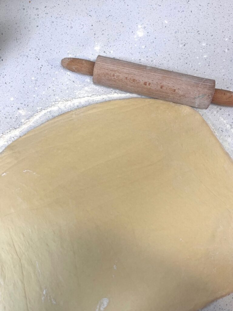 A large rectangle of dough rolled out onto a lightly floured countertop with a rolling pin.